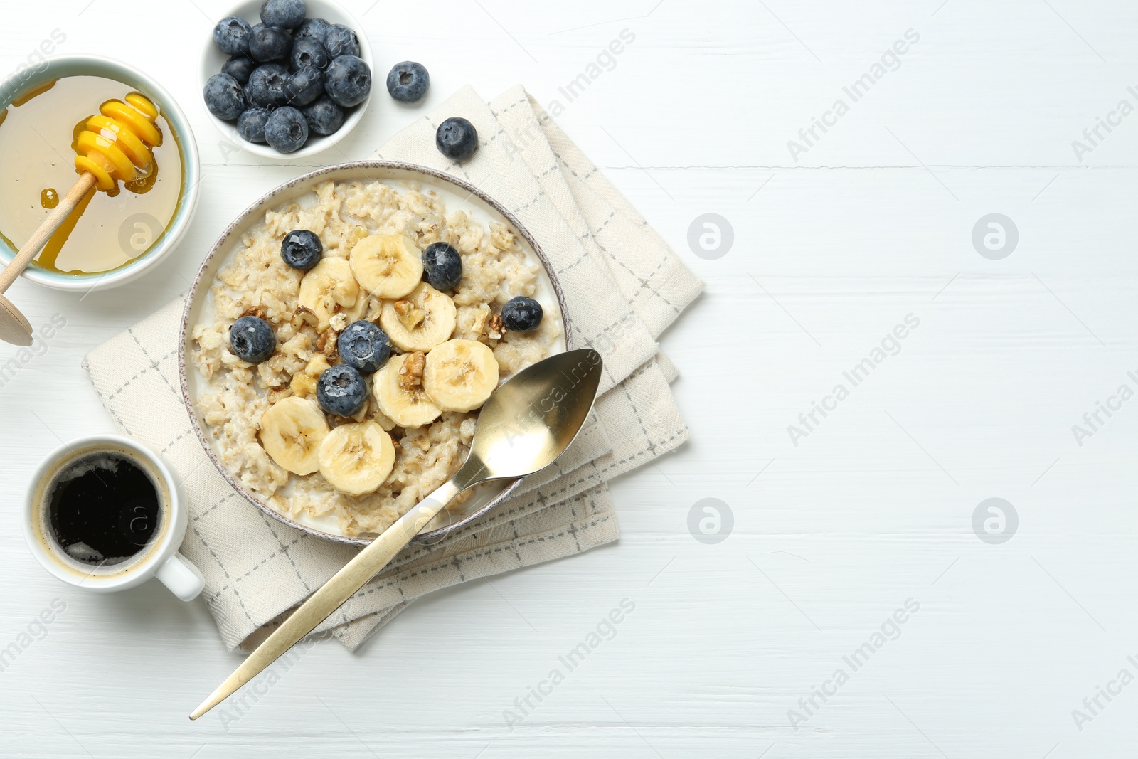 Photo of Tasty oatmeal with banana, blueberries, walnuts and honey served in bowl on white wooden table, flat lay. Space for text