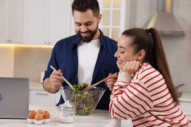 Photo of Happy lovely couple cooking together near laptop in kitchen