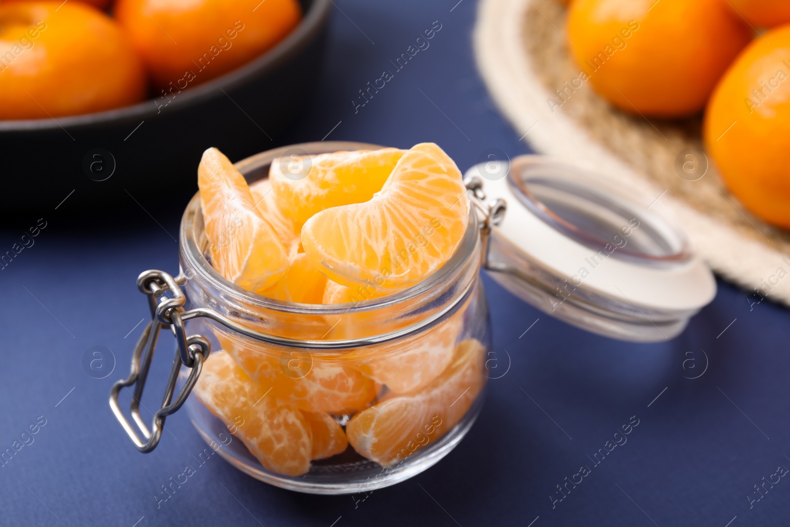 Photo of Glass jar of fresh juicy tangerine segments on blue table, space for text