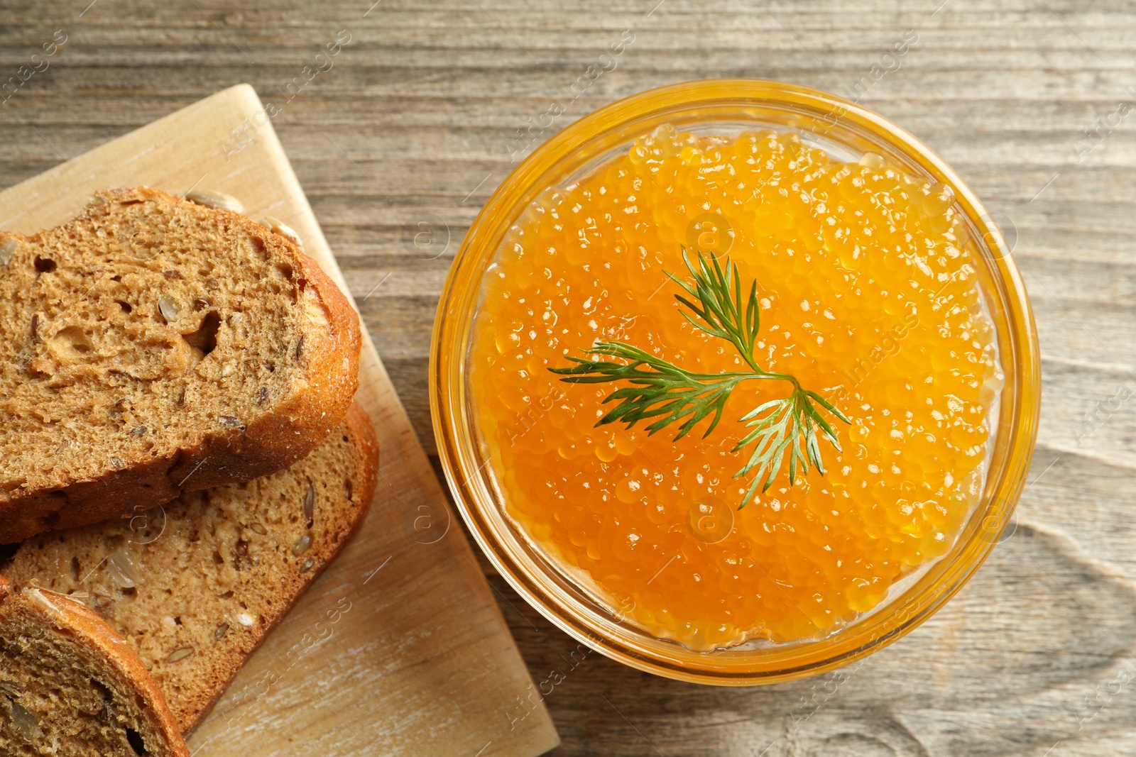 Photo of Fresh pike caviar in bowl and bread on wooden table, top view