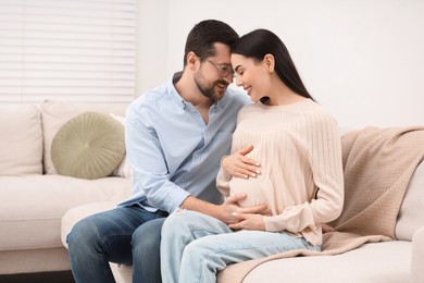 Photo of Happy pregnant woman with her husband on sofa at home