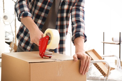 Photo of Young man packing moving box indoors, closeup