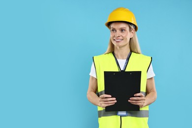 Photo of Engineer in hard hat holding clipboard on light blue background, space for text