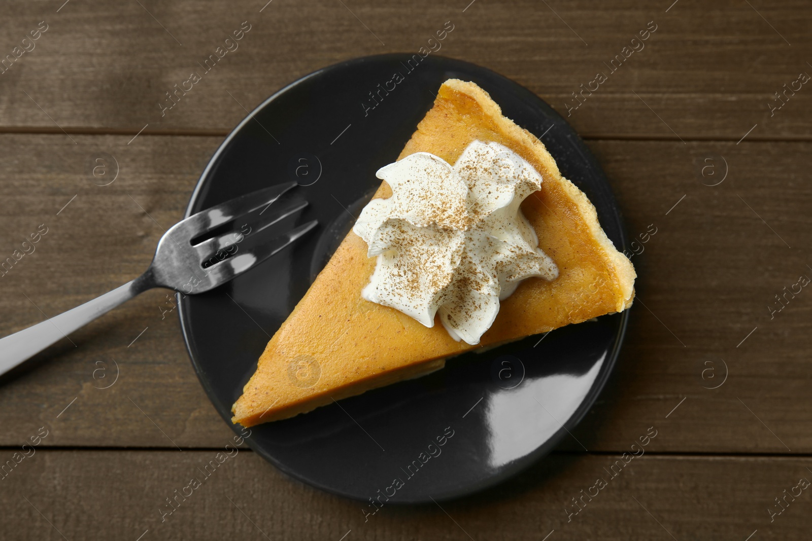 Photo of Piece of delicious pumpkin pie with whipped cream and fork on wooden table, top view