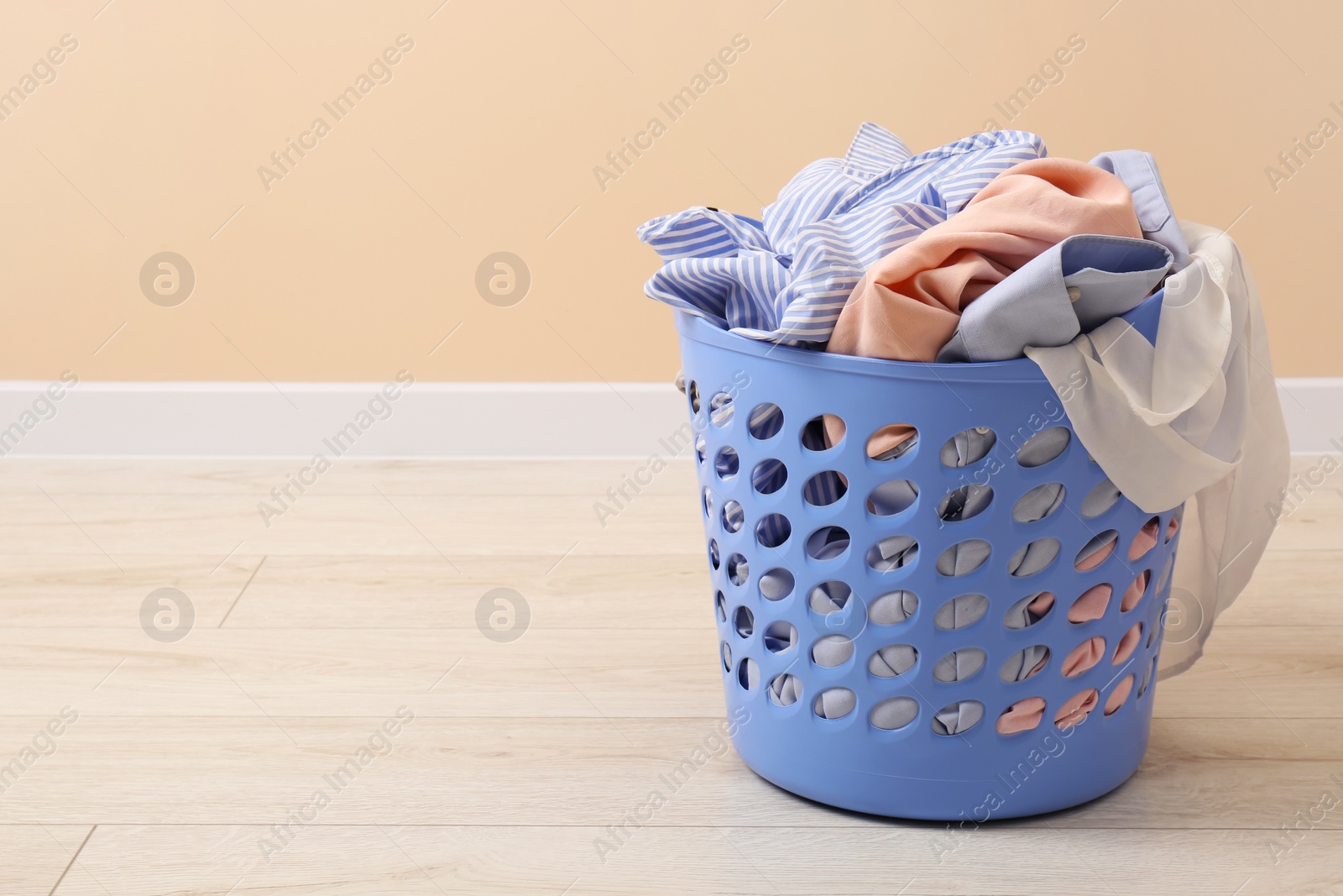 Photo of Laundry basket with clothes near beige wall indoors. Space for text