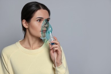 Photo of Sick young woman using nebulizer on grey background, space for text