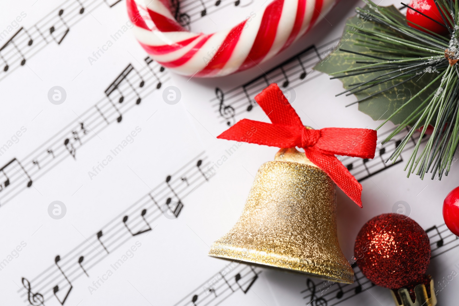 Photo of Golden shiny bell with red bow and Christmas decor on music sheets, flat lay