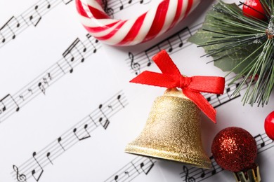 Photo of Golden shiny bell with red bow and Christmas decor on music sheets, flat lay