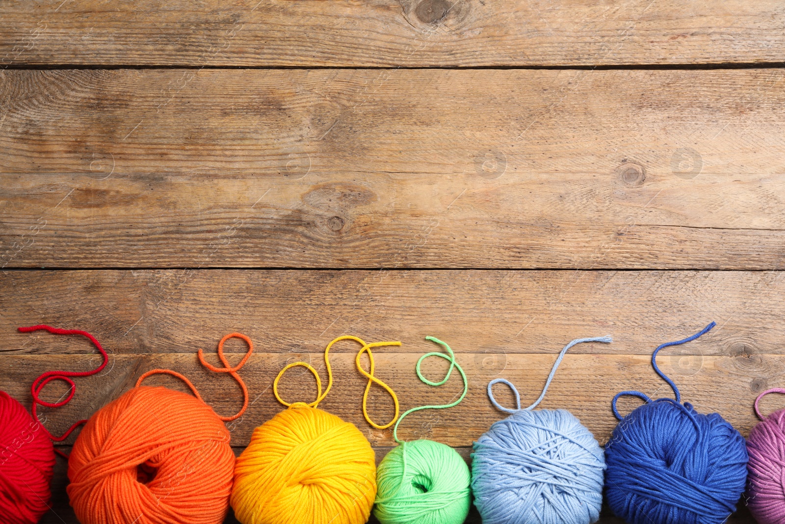 Photo of Soft colorful woolen yarns on wooden table, flat lay. Space for text