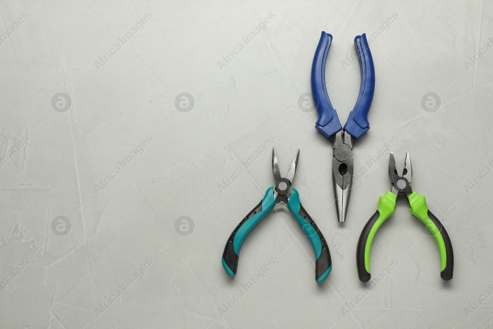 Photo of Different pliers on grey textured table, flat lay. Space for text