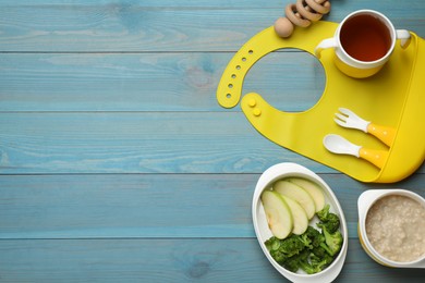 Photo of Silicone baby bib, toy and plastic dishware with healthy food on light blue wooden, flat lay. Space for text