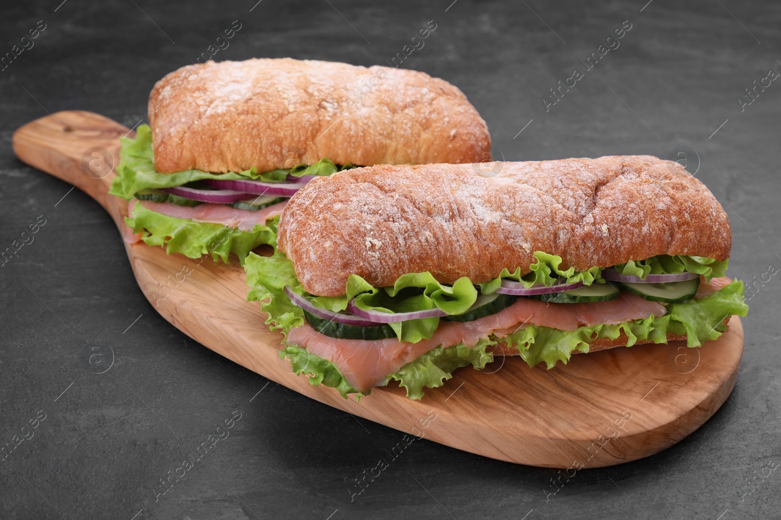 Photo of Delicious sandwiches with fresh vegetables and salmon on black table