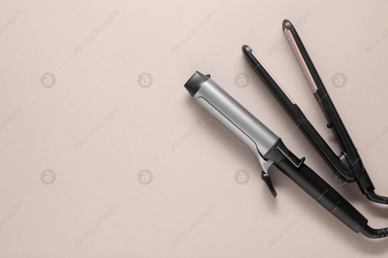 Photo of Curling iron and hair straightener on beige background, top view. Space for text