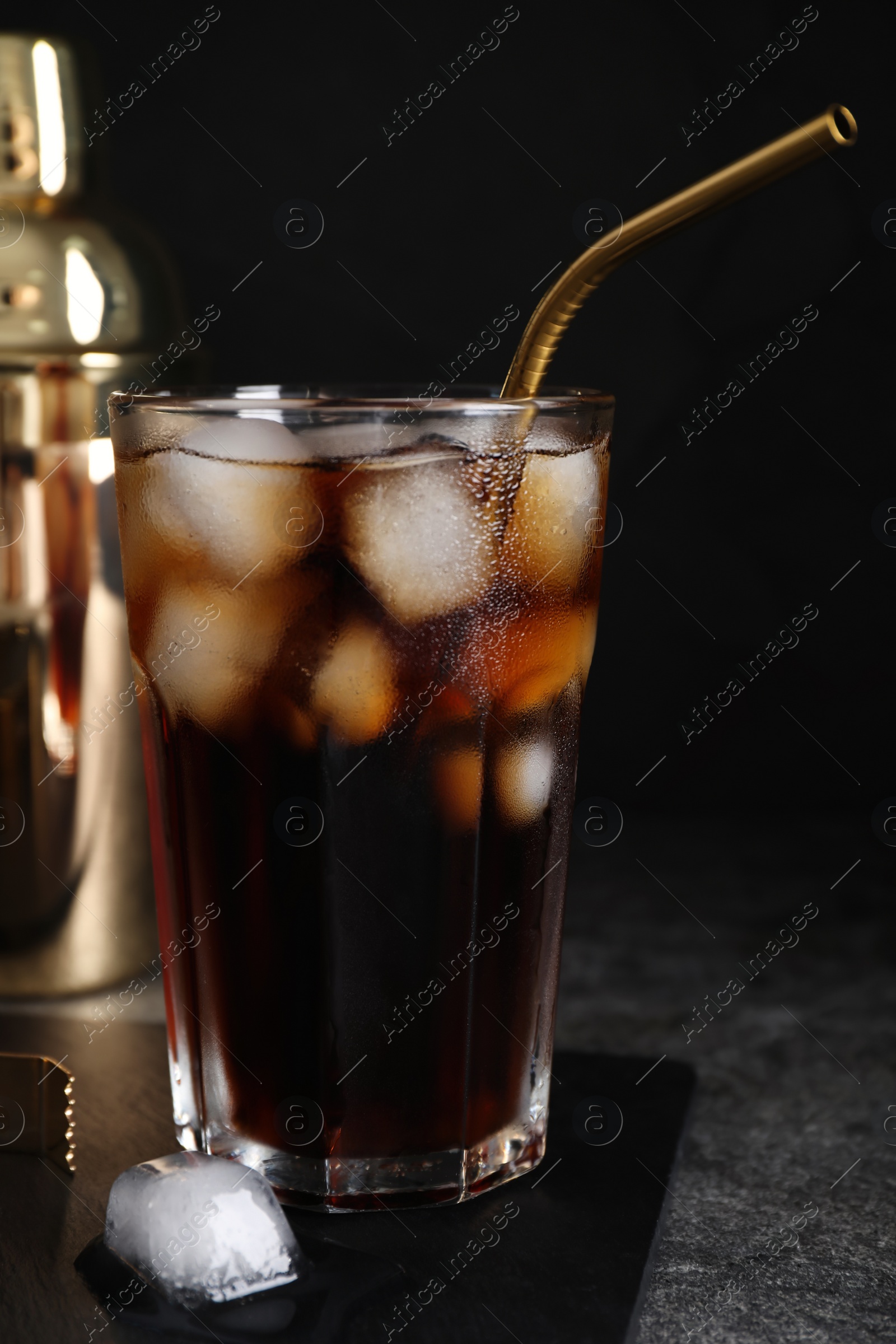 Photo of Tasty cola with ice cubes on grey table against dark background