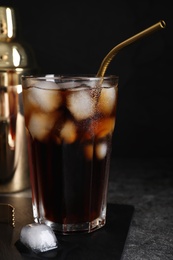 Tasty cola with ice cubes on grey table against dark background