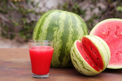 Photo of Delicious ripe watermelons and glass of fresh juice on wooden table outdoors