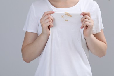 Woman showing stain on her t-shirt against light grey background, closeup