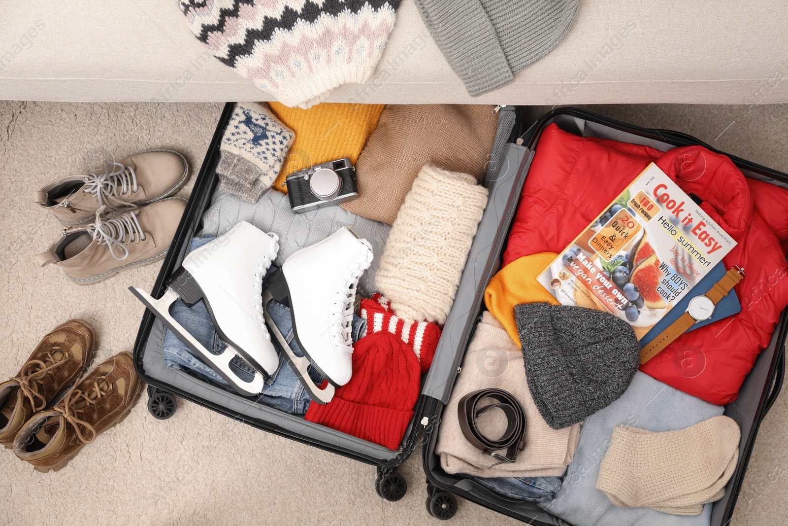 Photo of Open suitcase with warm clothes, accessories and shoes near sofa indoors, flat lay