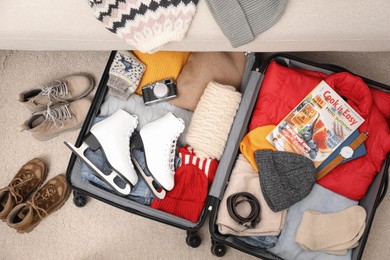 Photo of Open suitcase with warm clothes, accessories and shoes near sofa indoors, flat lay