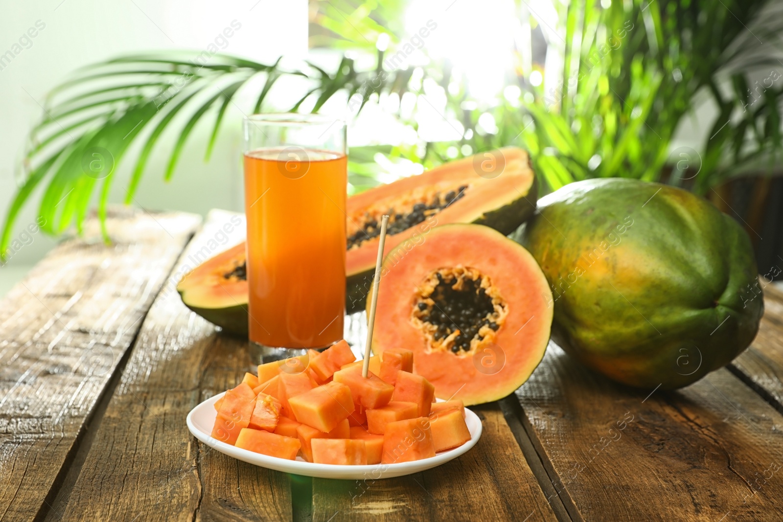 Photo of Fresh papayas and juice on wooden table against blurred background