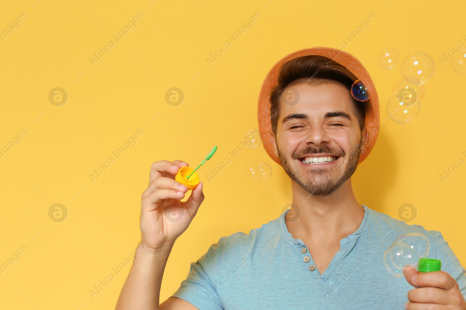 Photo of Young man blowing soap bubbles on color background. Space for text