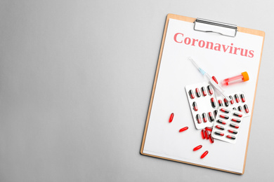 Photo of Clipboard with word CORONAVIRUS, test tube, syringe and medicine on light grey background, top view. Space for text