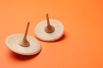 Photo of Two wooden spinning tops on orange background, space for text