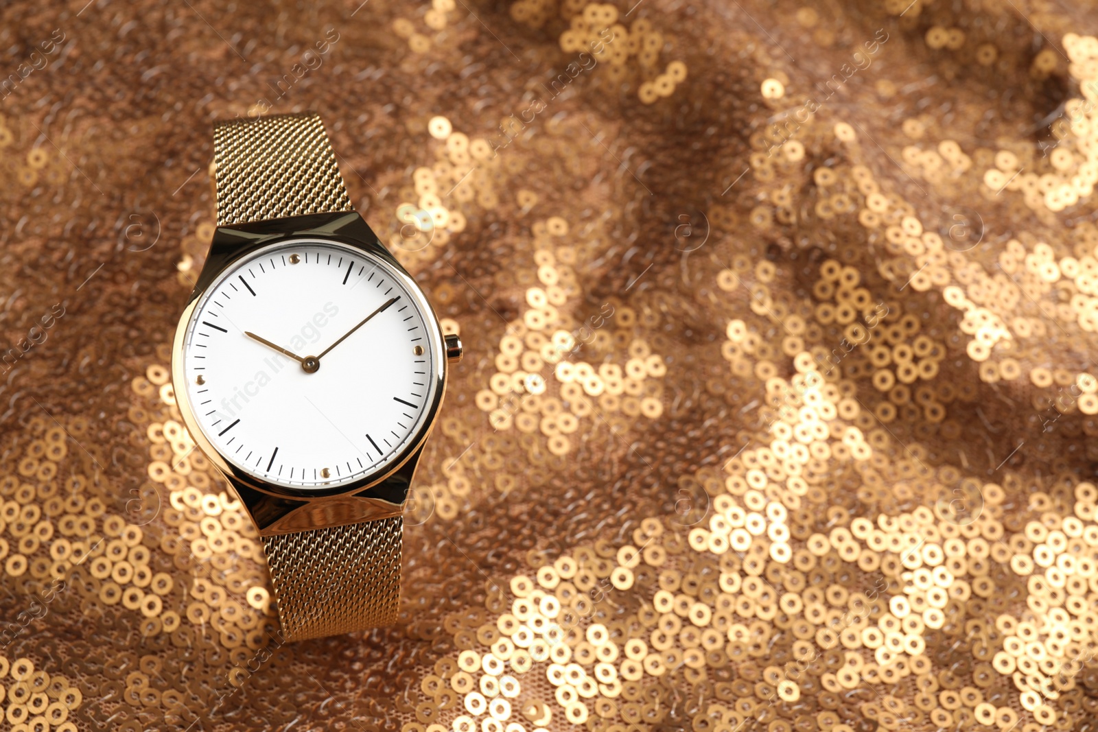 Photo of Luxury wrist watch on gold paillette background. Space for text