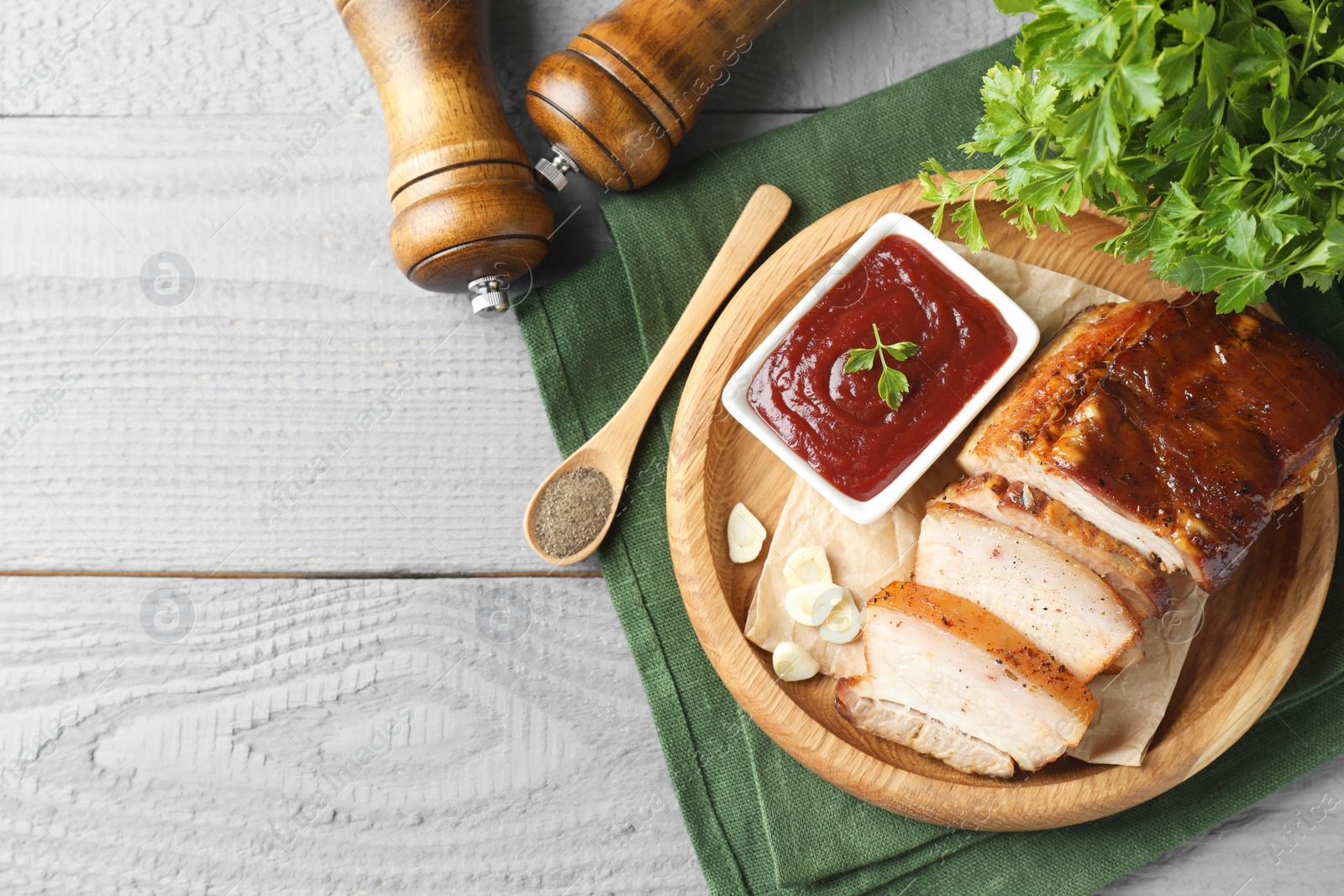 Photo of Pieces of baked pork belly served with sauce on grey wooden table, top view. Space for text