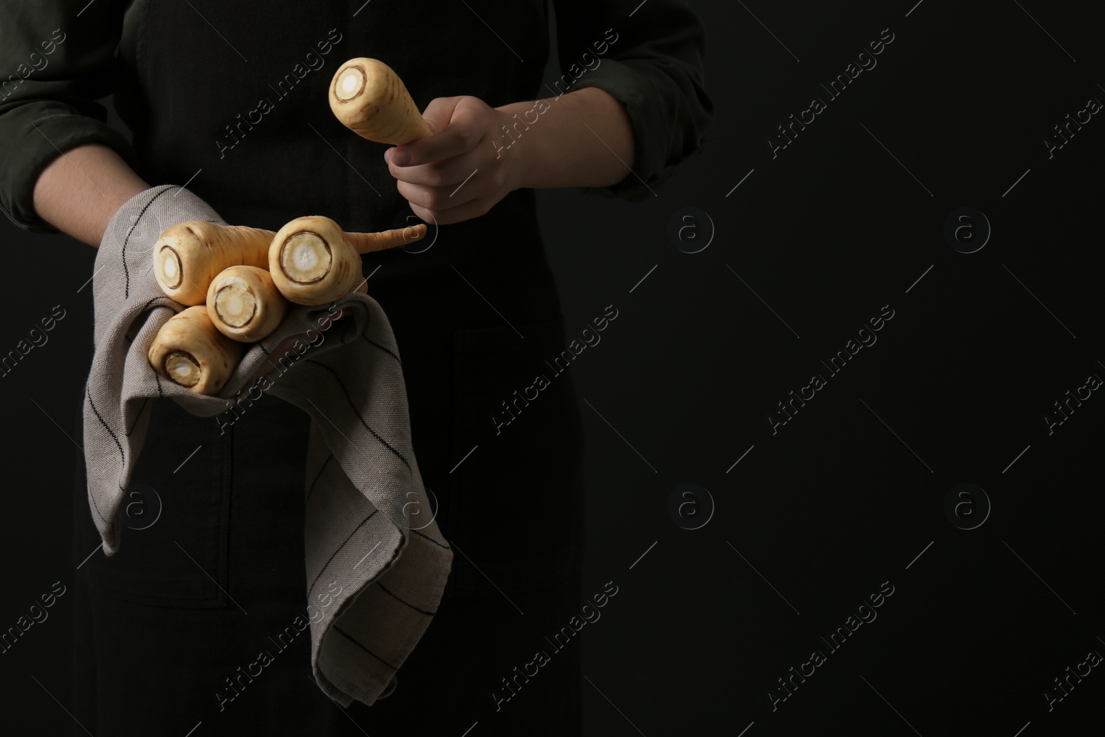 Photo of Woman holding fresh ripe parsnips on black background, closeup. Space for text