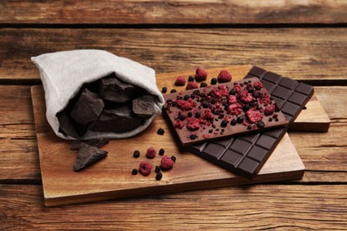 Photo of Board and different chocolate bars with freeze dried fruits on wooden table