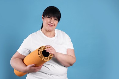 Photo of Happy overweight mature woman with yoga mat on light blue background. Space for text