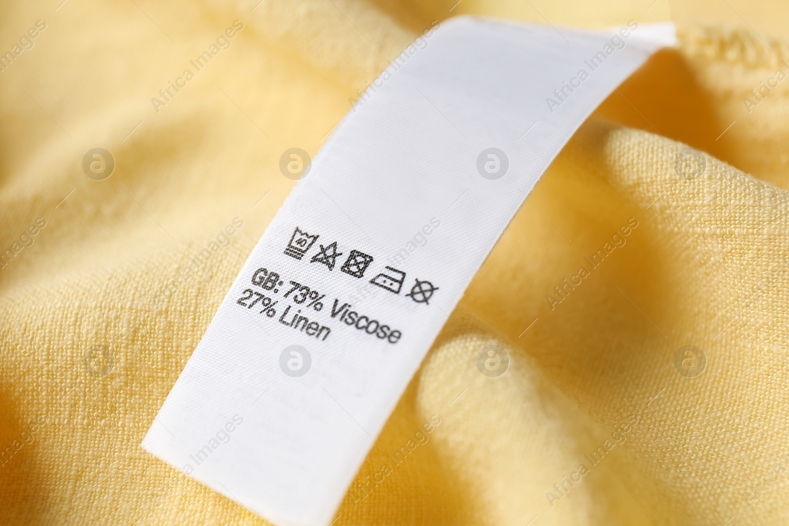 Photo of Clothing label with care symbols and material content on yellow shirt, closeup view