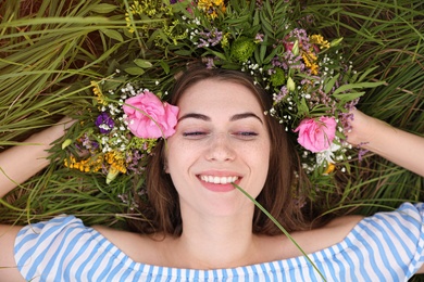 Young woman wearing wreath made of beautiful flowers on green grass, top view