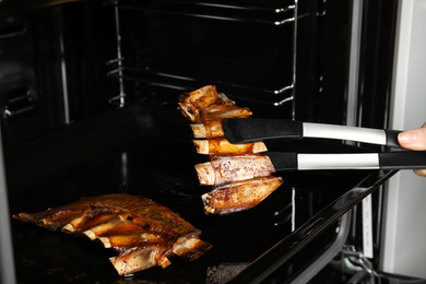 Woman taking delicious roasted ribs out of oven, closeup