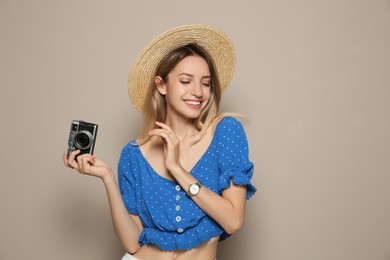 Photo of Beautiful young woman with straw hat and camera on beige background. Stylish headdress