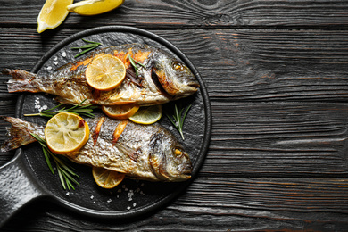 Photo of Delicious roasted fish with lemon on black wooden table, flat lay. Space for text