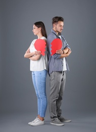 Young couple with torn paper heart on grey background. Relationship problems