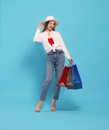 Photo of Stylish young woman with shopping bags on light blue background