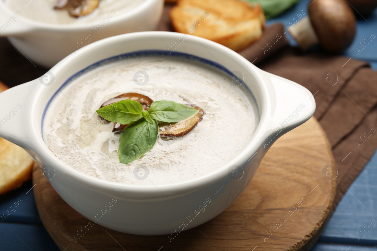 Photo of Fresh homemade mushroom soup in ceramic pot on blue wooden table, closeup
