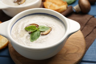 Fresh homemade mushroom soup in ceramic pot on blue wooden table, closeup