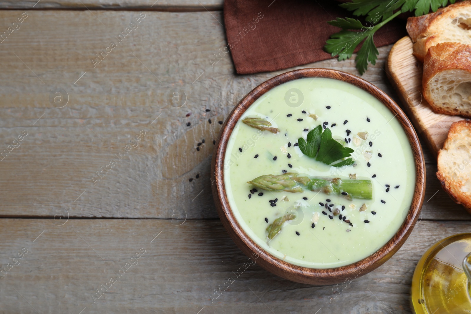 Photo of Bowl of delicious asparagus soup served on wooden table, flat lay. Space for text