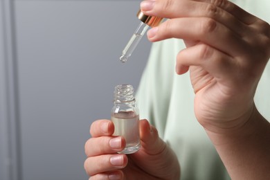 Photo of Woman with bottle of cosmetic serum and pipette on grey background, closeup. Space for text