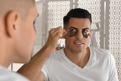 Photo of Man applying dark under eye patch near mirror at home