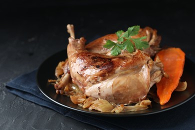 Photo of Tasty cooked rabbit meat with vegetables and parsley on black table, closeup. Space for text