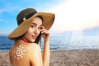 Young woman with sun protection cream on her back at beach, space for text