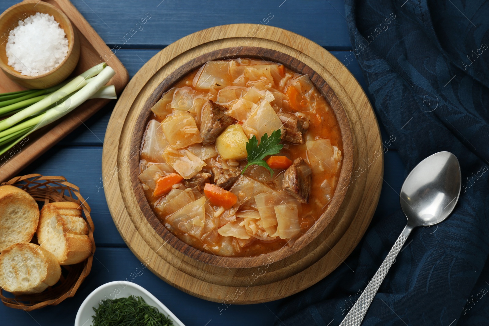 Photo of Tasty cabbage soup with meat, carrot and parsley served on blue wooden table, flat lay