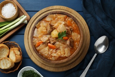 Photo of Tasty cabbage soup with meat, carrot and parsley served on blue wooden table, flat lay
