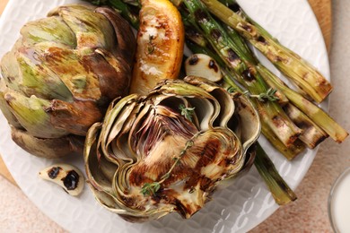 Photo of Plate with tasty grilled artichokes and asparagus on table, closeup