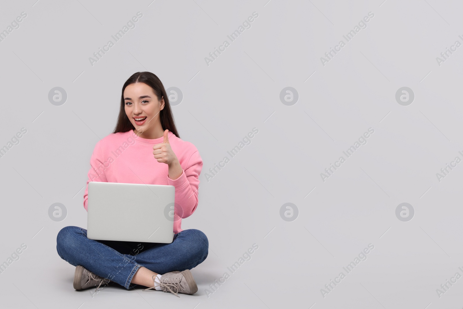 Photo of Smiling young woman with laptop showing thumbs up on grey background, space for text